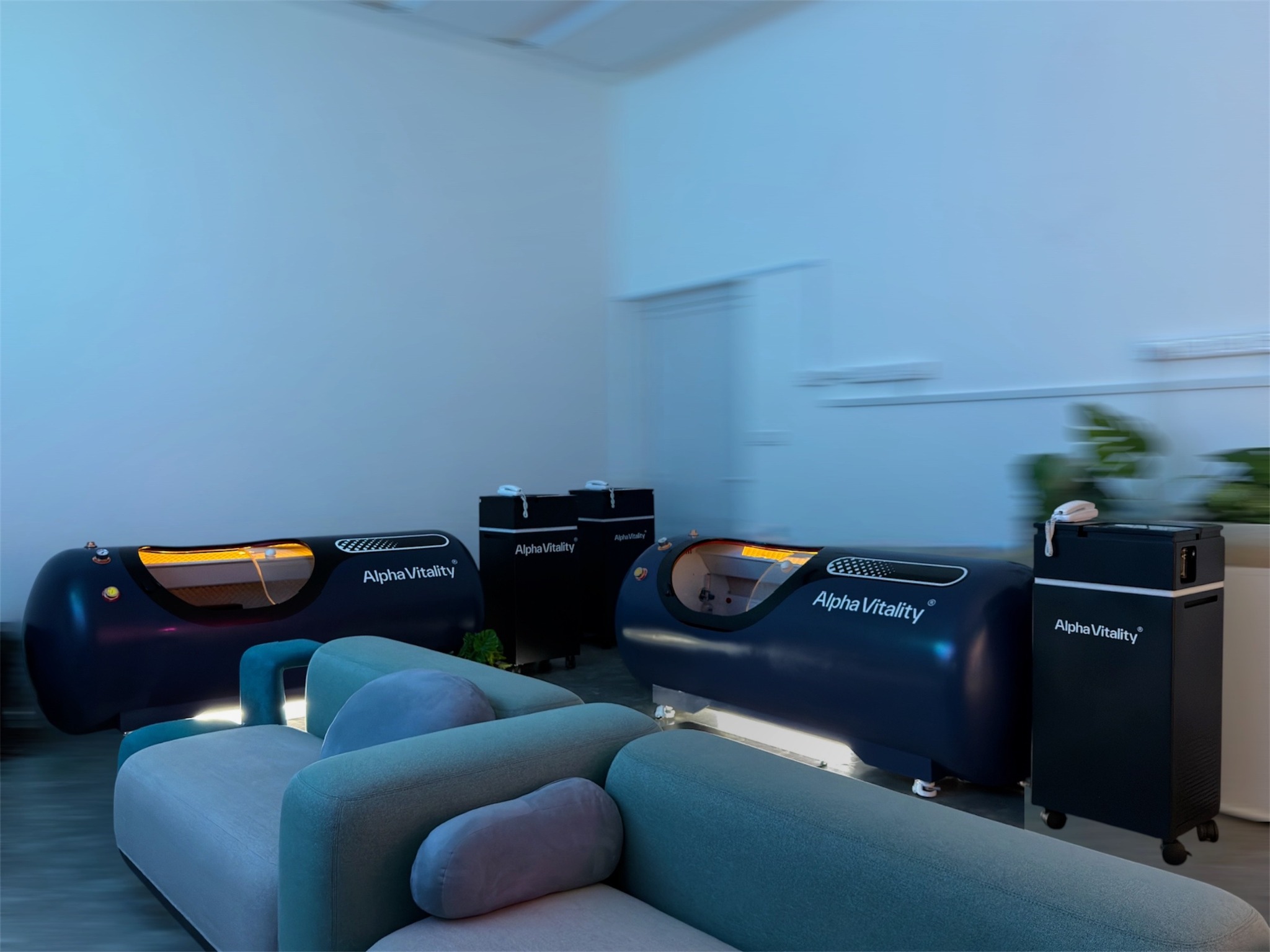 Two individual Alpha Vitality HBOT chambers beside lounge seating